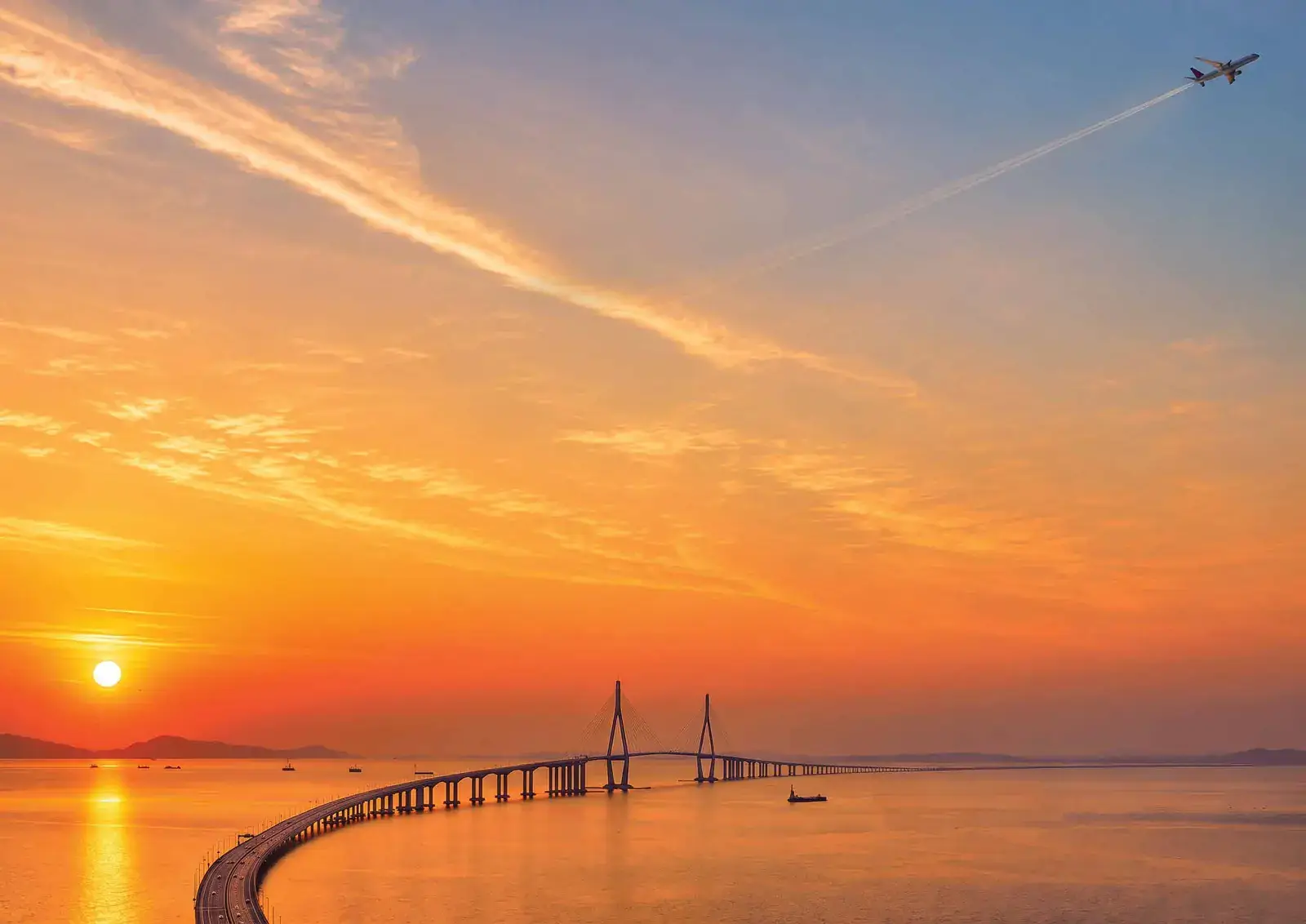 Cable-stayed sea bridge at sunset with a plane overhead: new sea-link and airport connectivity for the region (representative image)